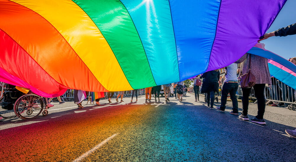  People marching with a large rainbow flag in a Gay Pride parade